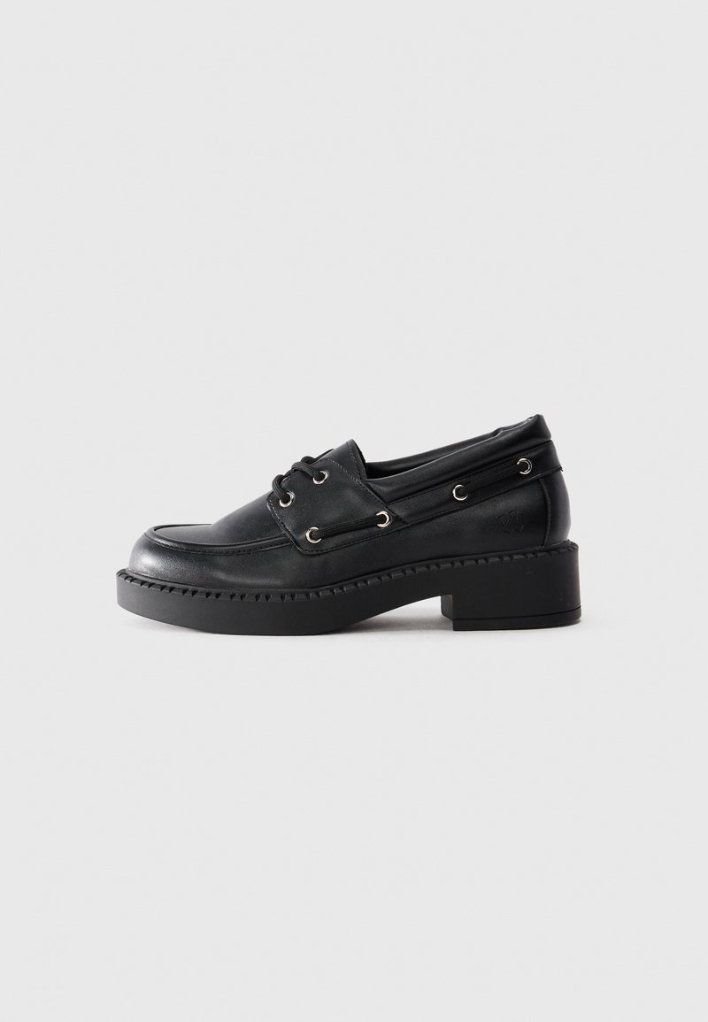 Loafer din piele neagră cu talpă groasă, față cu șireturi și toc mic pe un fundal simplu deschis.