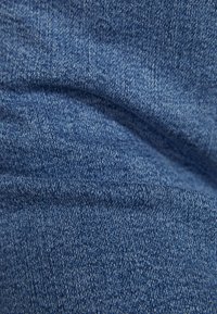 Närbild av blå denimtyg med synlig twillvävstruktur och mjuka veck.