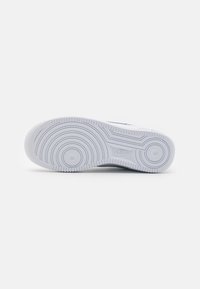 Hvit gummisåle til sneakers med sirkulære mønstre og en glatt overflate. Merkbar Nike-logo nær midtsålen.
