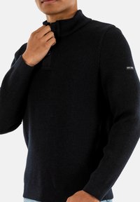 Maglione a coste ribbed blu navy con colletto alto, chiusura a bottoni e dettaglio con logo sulla manica. Texture morbida e design aderente.
