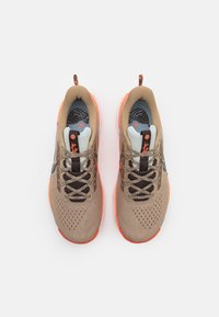 Un par de zapatillas de running en color marrón claro y naranja con cordones negros y plantillas estampadas, vistas desde arriba sobre un fondo blanco.