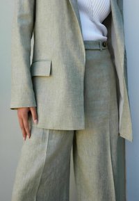 Světlý zelený lněný oblek s elegantním sáčkem a kalhotami širokého střihu. Materiál má jemnou texturu a obsahuje diskrétní vzor.