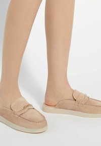 Beige suède instappers met een ronde neus, een laag profiel rubberen zool en een decoratieve band met een metalen accent.