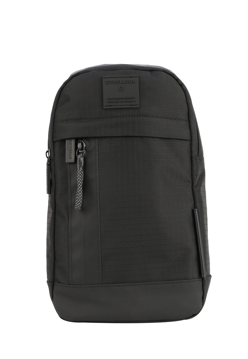 Črn nahrbtnik z teksturirano tkanino, sprednjim žepom na zadrgo, logotipom in trdno zasnovo z kontrastnim gladkim spodnjim delom.