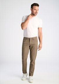 Camiseta blanca ligera combinada con pantalones ajustados marrones y zapatillas blancas. El conjunto presenta un diseño sencillo con corte recto.