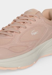 Baskets Lacoste rose clair avec panneaux en mesh et texturés, design à lacets, logo crocodile blanc et semelle blanche épaisse.
