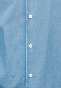 Ανοιχτό μπλε πουκάμισο με κουμπιά, φτιαγμένο από απαλό ύφασμα, με λευκά κουμπιά και λεία υφή, με κλασικό σχεδιασμό γιακά.