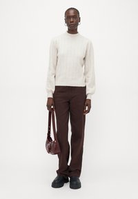 Pullover a coste di un beige chiaro con maniche lunghe, abbinato a pantaloni dritti marrone scuro. Tiene una borsa in pelle bordeaux. Scarpe chunky nere.