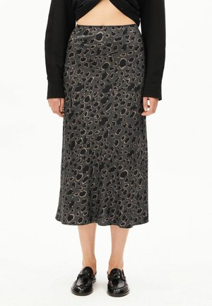 Kvinde iført en midt-lang mørkegrå nederdel med sort og brun leopardprint, sort top og sorte tassel loafers på hvid baggrund.