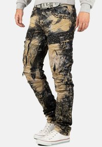 Pantaloni a fantasia marrone e neri con zip, dettagli borchiati e vestibilità slim, realizzati in denim con una texture consumata.