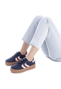 Sneakers blu navy con strisce rosa, realizzati in tessuto e gomma. Presentano una suola spessa color marrone e un design con lacci, con un motivo semplice.