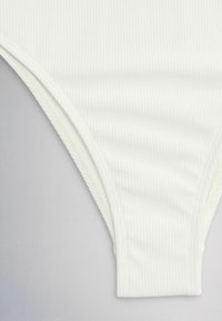 Gros plan sur un tissu blanc côtelé avec une couture courbée, probablement une partie d'un vêtement tel que des sous-vêtements ou un maillot de bain.