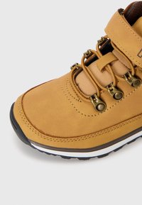Bota de senderismo marrón con un upper de cuero texturizado, ganchos de metal para los cordones y una suela de goma que presenta una franja blanca de acento.