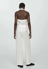 Salopetă albă, fără bretele, cu un corset conturat, pantaloni larghi, din material texturat și talie evidențiată cu curea; purtată cu pantofi negri cu vârf deschis.