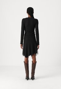 Svart stickad långärmad topp med ribbad textur, kombinerad med en svart kjol med genomskinlig fåll. Bruna cowboyboots med spetsiga tår.