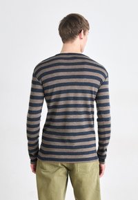 Chemise à manches longues rayée bleu marine et beige. Fabriquée dans un matériau doux avec un col rond et une coupe ajustée, assortie à un pantalon vert olive.