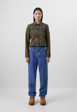 Brown denim jacket with a zip front, chest pocket, and tonal stitching; paired with light blue loose-fitting jeans and tan boots.