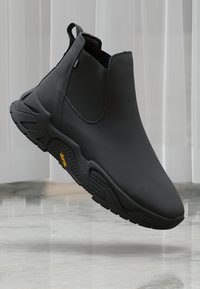 Black ankle boots with a sleek design, showcased against a light backdrop, highlighting their modern style and textured sole.