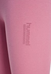 Gros plan d'un tissu de sport rose avec le logo en relief "hummel SPORTSWEAR" sur la zone de la cuisse.
