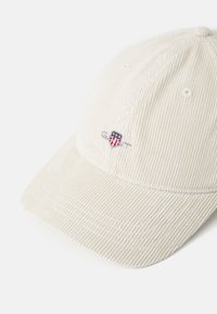Beige corduroy cap with a curved brim, featuring a small embroidered logo on the front and stitched detailing on the visor.