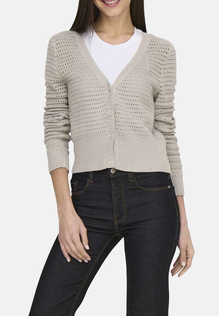 Cardigan en tricot beige clair avec un col en V, six boutons et des poignets côtelés. Présente un design perforé et associé à un jean foncé.