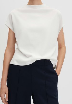 Haut blanc à manches courtes avec un col montant et une texture douce, associé à un pantalon bleu marine foncé sur mesure, présentant un design simple et épuré.