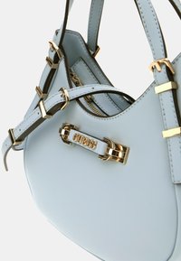 Borsa a mano in pelle azzurro chiaro con hardware dorato, placca con logo prominente e manici regolabili. Texture liscia e forma arrotondata.