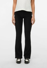 Pantalons évasés noirs en tissu extensible, ajustés au niveau des cuisses et avec un bas plus large. Finition avec un matériel minimal.
