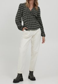 Blusa avvolgente a maniche lunghe con motivo in bianco e nero, abbinata a pantaloni bianchi a gamba dritta e stivali neri chunky alla caviglia.