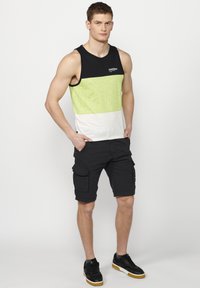 Juodas ir neono žalias marškinėlių topas su horizontaliomis juostelėmis, derinamas su juodais kargo šortais. Marškinėliai turi logotipą ant krūtinės ir laisvą siluetą.