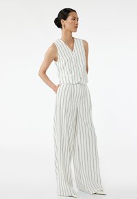 Biała bezrękawnik z niebieskimi pionowymi paskami, z guzikami i kieszeniami, w połączeniu z szerokimi spodniami w paski. Gładka struktura materiału.