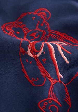 Mörkblått tyg med intrikata röda broderier av en björn, som visar detaljerade ansiktsdrag och tassar, med en mjuk textur.