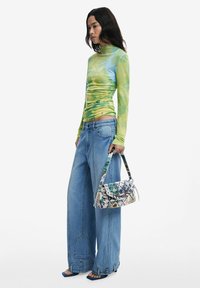 Langärmliges, grün-blaues Batik-Oberteil; lockere, hellblaue Jeans; bedruckte Handtasche; blaue Sandalen mit offenen Zehen.