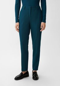 Turkusowe dopasowane spodnie o gładkiej fakturze, z płaskim przodem, dwoma bocznymi kieszeniami i smukłym, prostym krojem nogawek. Zestawione z czarnymi mokasynami.