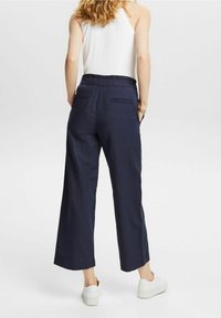 Mörkblå vida byxor i lätt tyg med elastisk midja. Har två bakfickor och en avslappnad passform. Kombineras med vita sneakers.