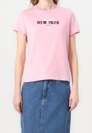 Kobieta ubrana w różowy t-shirt z krótkim rękawem z napisem "New York" i wzorem serca, w połączeniu z niebieską spódnicą dżinsową.