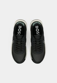 Ζεύγος μαύρων παπουτσιών BOSS με λευκές σόλες, μαύρα κορδόνια και το λογότυπο εμφανές στις πλευρές και στα πέλματα των παπουτσιών, εμφανιζόμενα από την κορυφή.