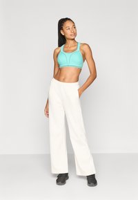 Τιρκουάζ αθλητικό σουτιέν με δομημένο σχέδιο και ελαστική ταινία, σε συνδυασμό με χαλαρά κρεμ φόρμες. Μαύρα αθλητικά παπούτσια ολοκληρώνουν την εμφάνιση.