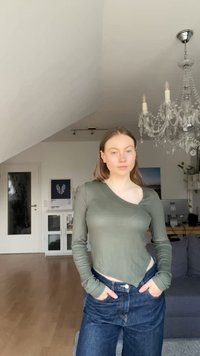 Langärmliges, olivgrünes Oberteil mit asymmetrischem Ausschnitt, kombiniert mit hochgeschnittenen, dunkelblauen Jeans. Glatter Stoff und taillierte Passform.