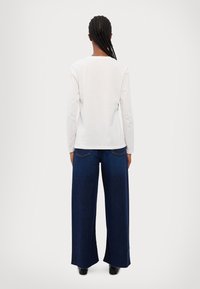 Camicia bianca a maniche lunghe abbinata a jeans blu scuro a vita alta e gamba larga, con tasche posteriori e orlo risvoltato.