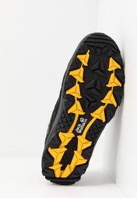 Suola di scarpa da esterno nera con un prominente motivo di trazione giallo e superficie texturizzata. Presenta il logo del marchio in bianco. Materiale in gomma durevole.