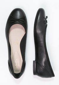 Ballerines noires en matériau synthétique lisse, avec un accent nœud sur le bout, semelle rembourrée et design arrondi élégant.