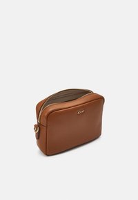 Trousse de maquillage en cuir brun avec une texture lisse, de forme arrondie, fermée par une fermeture éclair dorée et portant un logo en relief sur le devant. S'ouvre sur un intérieur beige.