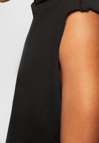 Black sleeveless top with a soft texture, featuring a round neckline and subtle stitching details along the armhole and hem.
