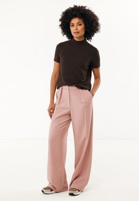Bruine sweater met korte mouwen, gecombineerd met lichtroze wijde broek. De outfit heeft gladde texturen en een relaxte pasvorm. Aangevuld met donkere schoenen.