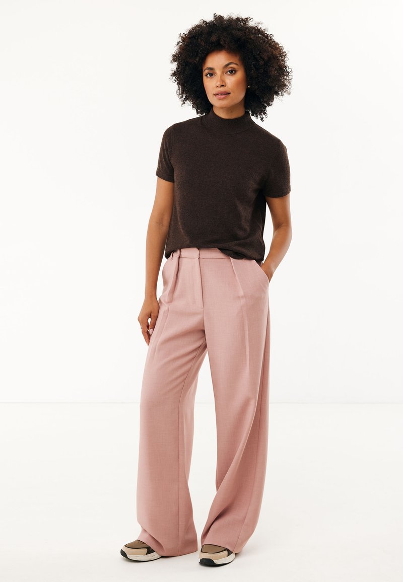 Brązowy sweter z krótkim rękawem w połączeniu z jasnoróżowymi szerokimi spodniami. Strój charakteryzuje się gładkimi teksturami i luźnym krojem. Podkreślony ciemnym obuwiem.