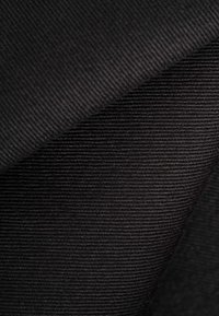 Close-up of folded black corduroy fabric showing diagonal ridged texture and fine vertical lines.