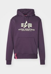 Sweat à capuche violet avec cordons, présentant une poche avant et un imprimé de logo. Le tissu semble doux avec des poignets et une taille côtelés.