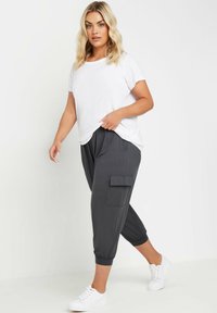 Witte t-shirt met korte mouwen gecombineerd met donkergrijze cropped broek met een zijzak en elastische boorden, gedragen met witte sneakers.