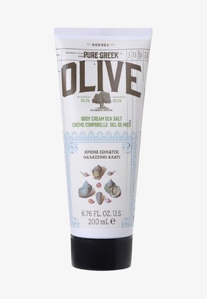 Weißes Röhrchen mit einem helllila Deckel. Das Vorderetikett zeigt "OLIVE" in fettem Grau und weist auf "KÖRPERCREME MEERSALZ" in Grün hin, begleitet von Muschelillustrationen.